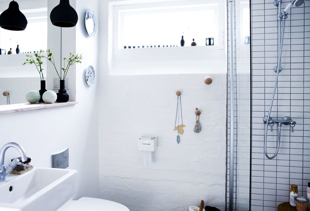 Veggene på badet er av ren, hvit mur, inne i dusjen er det derimot små fliser. Vinduet er høyt plassert på veggen, slik at dagslyset kommer inn, men man slipper innsyn. Badet har ikke et baderomsmøbel, men bare en enkel vask, og en trehylle under speilet. FOTO: Tia Borgsmidt